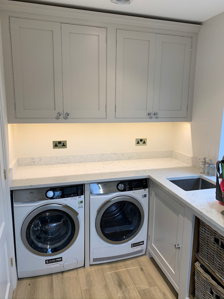Photo of a mid-sized contemporary l-shaped laundry room in Surrey with beaded inset cabinets, quartzite benchtops, mirror splashback and white benchtop.