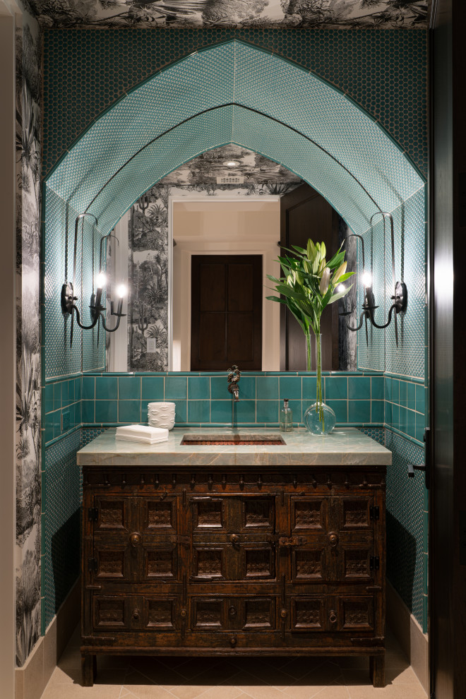 Пример оригинального дизайна: туалет в средиземноморском стиле с темными деревянными фасадами, синей плиткой, разноцветными стенами, врезной раковиной, бежевым полом, зеленой столешницей, напольной тумбой и обоями на стенах