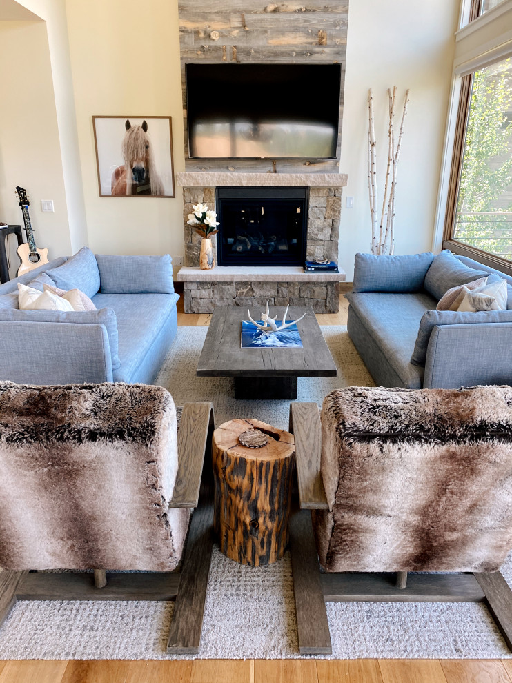 Inspiration for a large modern open concept living room in Denver with white walls, light hardwood floors, a standard fireplace, a stone fireplace surround, a wall-mounted tv, beige floor and vaulted.