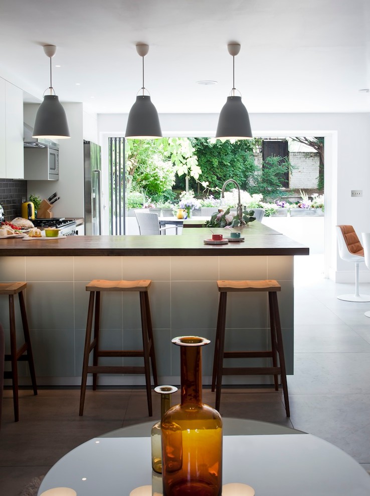 Inspiration for a contemporary u-shaped open plan kitchen in London with flat-panel cabinets, subway tile splashback, black splashback and stainless steel appliances.