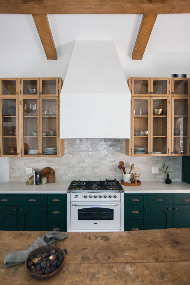 This is an example of a mid-sized mediterranean galley open plan kitchen in Los Angeles with flat-panel cabinets, green cabinets, quartz benchtops, white splashback, subway tile splashback, panelled appliances, ceramic floors, no island, black floor and white benchtop.