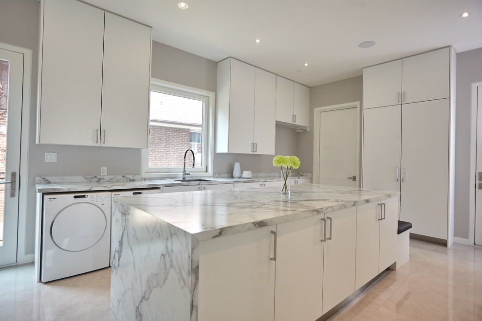 Expansive modern l-shaped utility room in Toronto with an undermount sink, flat-panel cabinets, white cabinets, quartzite benchtops, grey walls, a side-by-side washer and dryer and brown floor.