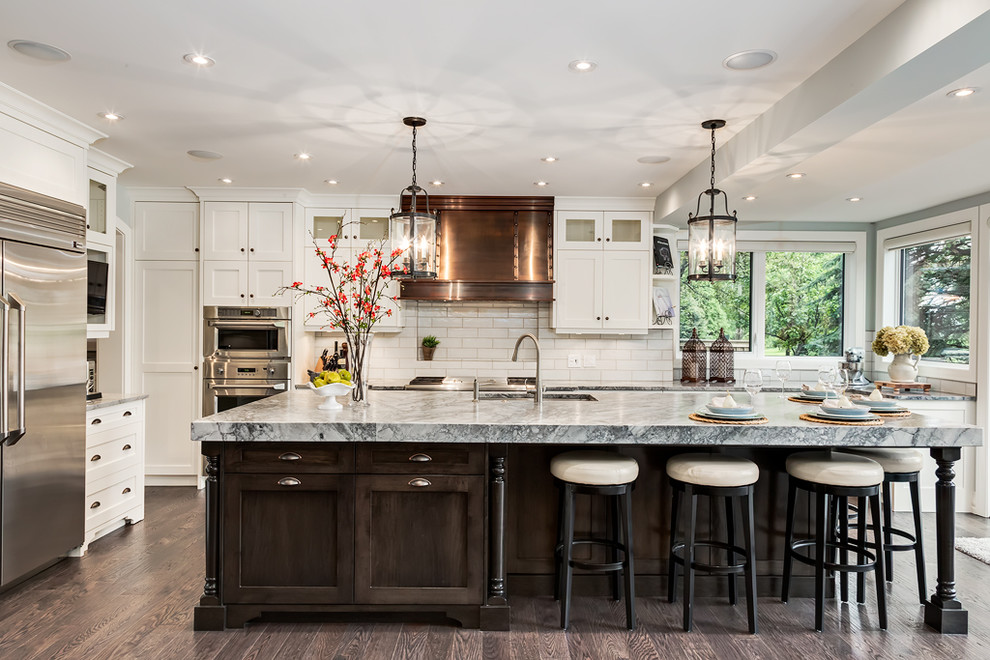 Inspiration for a mid-sized transitional l-shaped dark wood floor and brown floor enclosed kitchen remodel in Calgary with an undermount sink, shaker cabinets, white cabinets, white backsplash, subway tile backsplash, stainless steel appliances and an island