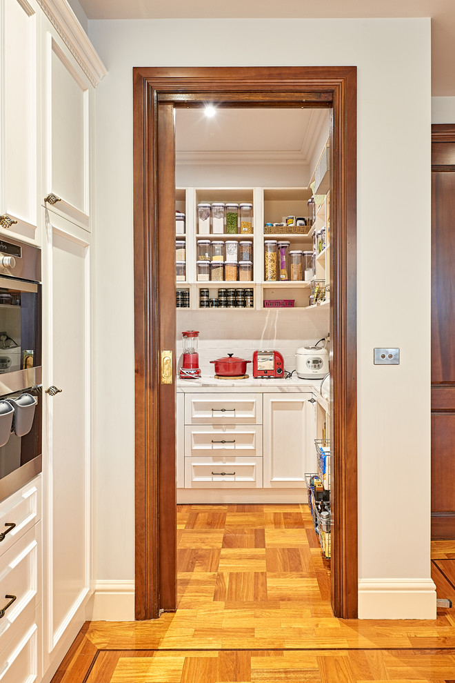 Photo of a mid-sized traditional l-shaped kitchen pantry in Melbourne with an undermount sink, shaker cabinets, white cabinets, solid surface benchtops, white splashback, subway tile splashback, stainless steel appliances, medium hardwood floors, with island and brown floor.