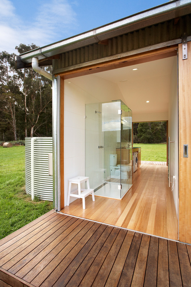 Industrial bathroom in Melbourne with a curbless shower, a two-piece toilet, white tile, ceramic tile, white walls, light hardwood floors and a laundry.