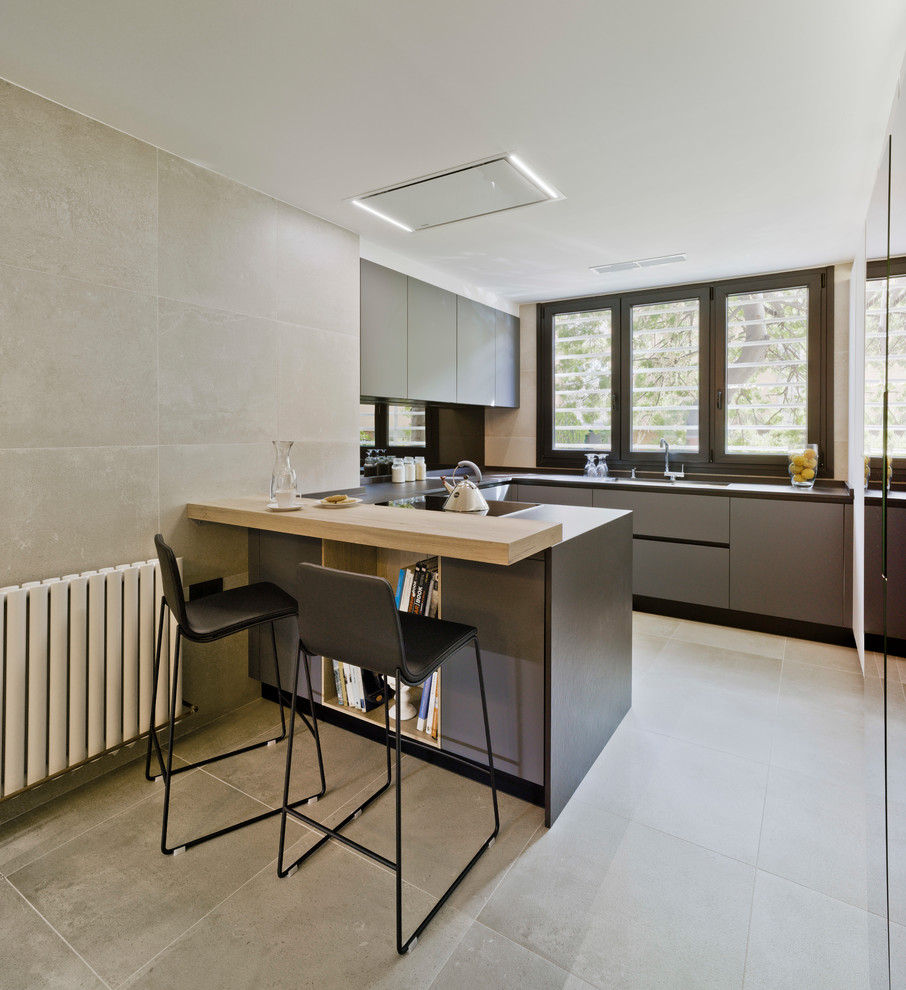 This is an example of a mid-sized contemporary u-shaped kitchen in Madrid with flat-panel cabinets, grey cabinets, a peninsula, grey floor, wood benchtops and black splashback.
