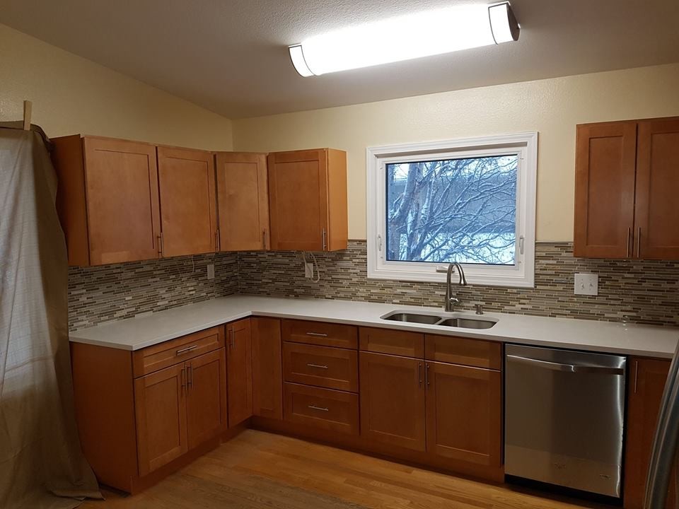 Kitchen - mid-sized transitional light wood floor kitchen idea with a double-bowl sink, shaker cabinets, light wood cabinets, solid surface countertops, multicolored backsplash and matchstick tile backsplash