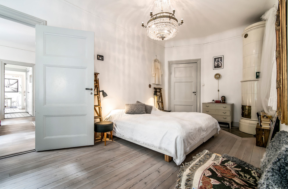 Design ideas for a mid-sized scandinavian master bedroom in Stockholm with white walls, medium hardwood floors and a corner fireplace.