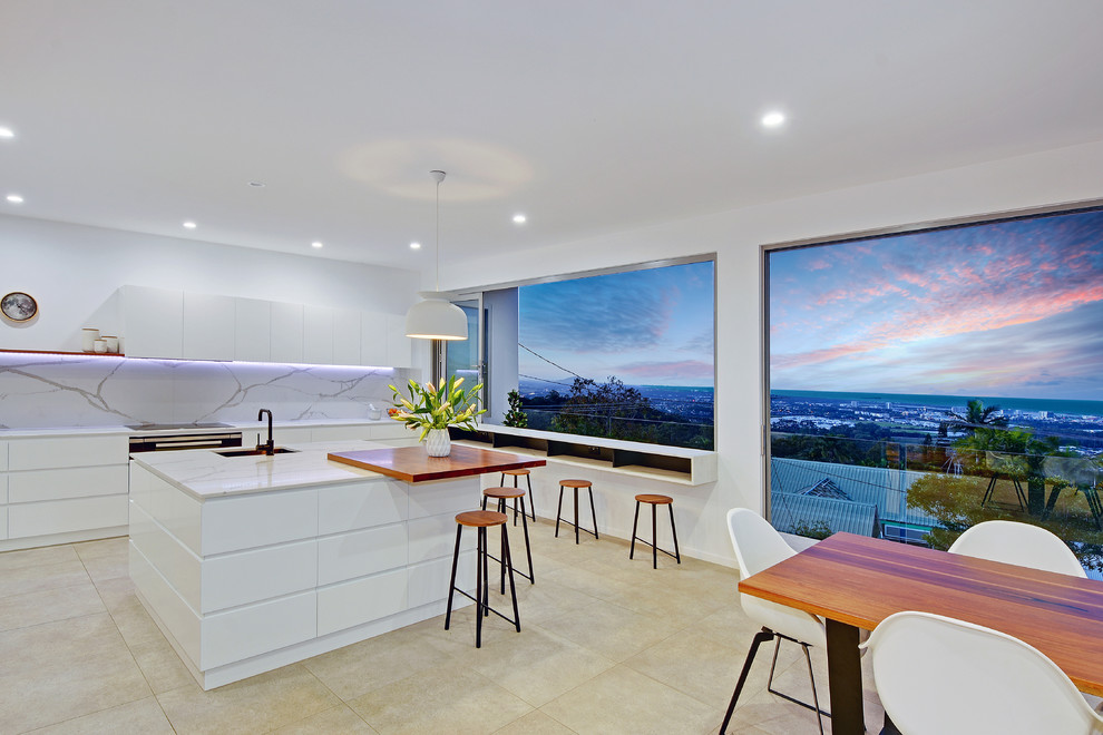 Photo of a large modern l-shaped open plan kitchen in Sunshine Coast with with island, a single-bowl sink, flat-panel cabinets, white cabinets, limestone benchtops, grey splashback, marble splashback, stainless steel appliances, beige floor and white benchtop.