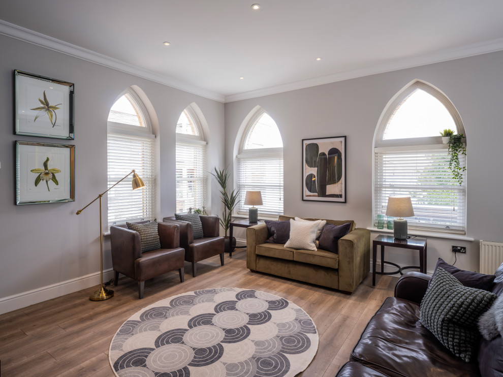 На фото: открытая гостиная комната в современном стиле с серыми стенами, полом из ламината и коричневым полом с