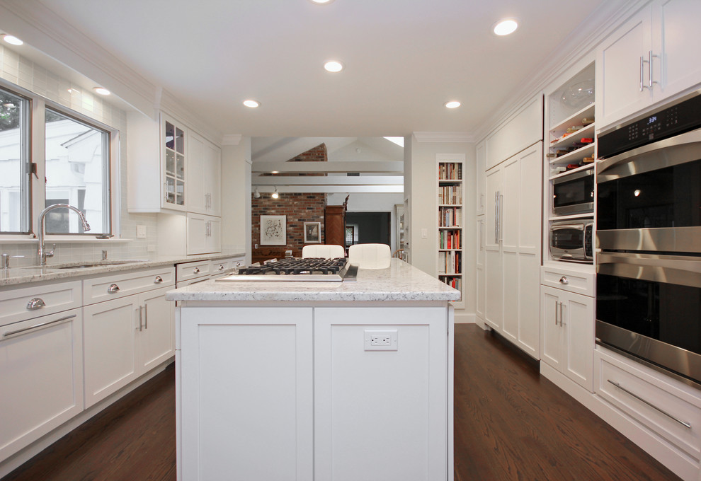 This is an example of a mid-sized transitional single-wall kitchen pantry in New York with with island, a drop-in sink, white cabinets, soapstone benchtops, white splashback, ceramic splashback, stainless steel appliances, medium hardwood floors, brown floor, white benchtop, vaulted and raised-panel cabinets.