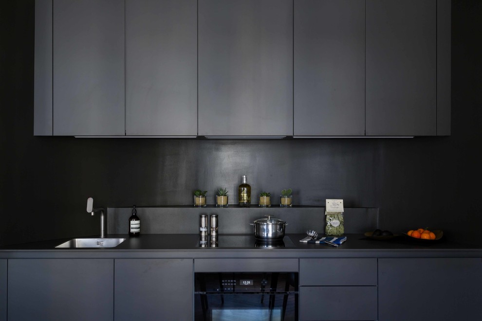 This is an example of a small contemporary single-wall open plan kitchen in Paris with a single-bowl sink, beaded inset cabinets, black cabinets, laminate benchtops, black splashback, panelled appliances, light hardwood floors, no island, brown floor and black benchtop.