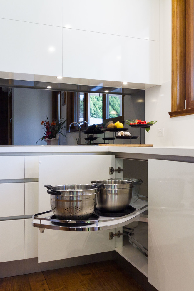 This is an example of a large contemporary u-shaped eat-in kitchen in Melbourne with an undermount sink, flat-panel cabinets, quartz benchtops, mirror splashback, stainless steel appliances, medium hardwood floors and with island.