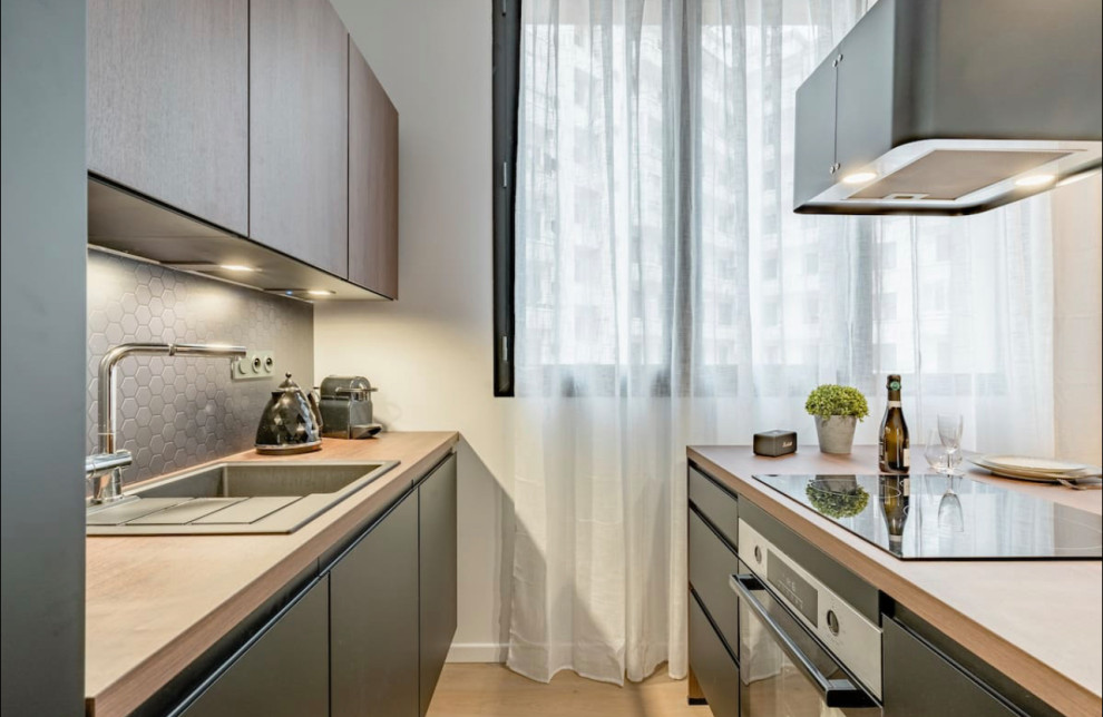 Small contemporary single-wall open plan kitchen in Lyon with an undermount sink, flat-panel cabinets, black cabinets, wood benchtops, grey splashback, ceramic splashback, panelled appliances, light hardwood floors, with island, beige floor and beige benchtop.