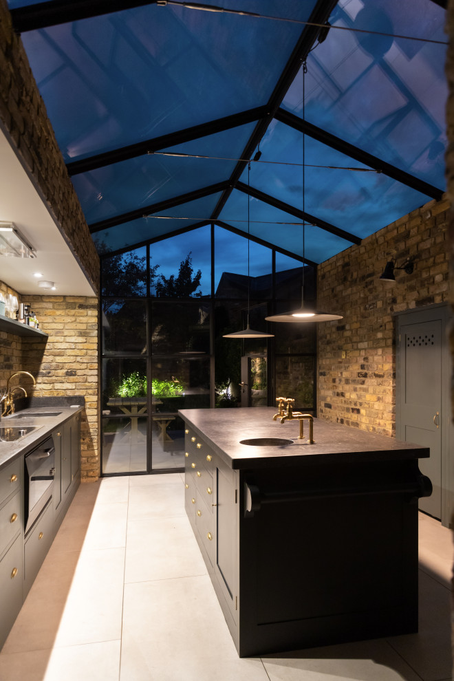 Photo of a small urban galley enclosed kitchen in London with a built-in sink, flat-panel cabinets, green cabinets, granite worktops, beige splashback, brick splashback, integrated appliances, limestone flooring, an island, beige floors and black worktops.