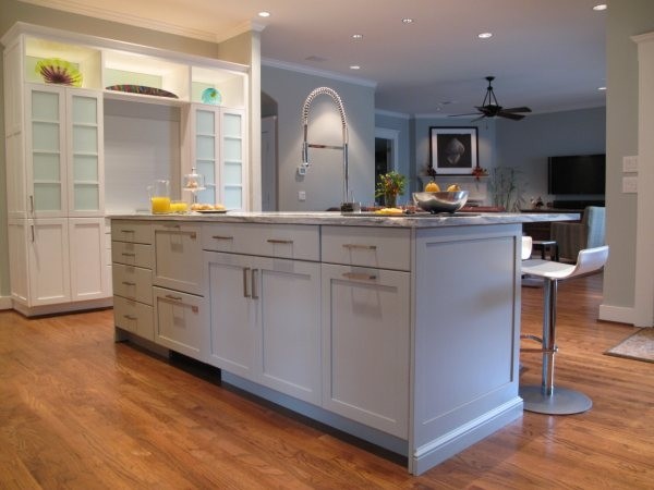This is an example of a mid-sized beach style l-shaped eat-in kitchen in Dallas with glass-front cabinets, white cabinets, grey splashback, glass tile splashback, stainless steel appliances, with island, a double-bowl sink, marble benchtops and light hardwood floors.