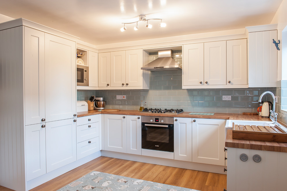Design ideas for a large country u-shaped open plan kitchen in Manchester with a farmhouse sink, recessed-panel cabinets, laminate benchtops, blue splashback, porcelain splashback, stainless steel appliances, vinyl floors and no island.