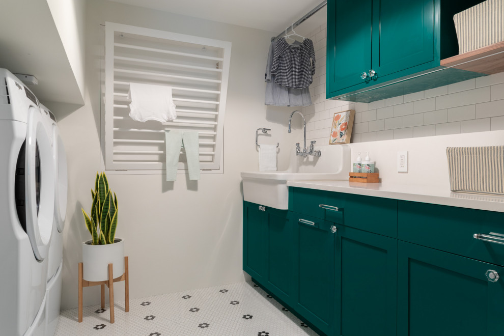 Mid-sized transitional galley dedicated laundry room in New York with a farmhouse sink, shaker cabinets, green cabinets, quartz benchtops, white splashback, engineered quartz splashback, white walls, ceramic floors, a side-by-side washer and dryer, white floor and white benchtop.