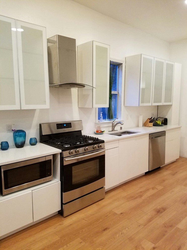 This is an example of a small transitional single-wall open plan kitchen in San Francisco with an undermount sink, glass-front cabinets, white cabinets, stainless steel appliances, medium hardwood floors, no island, brown floor and white benchtop.