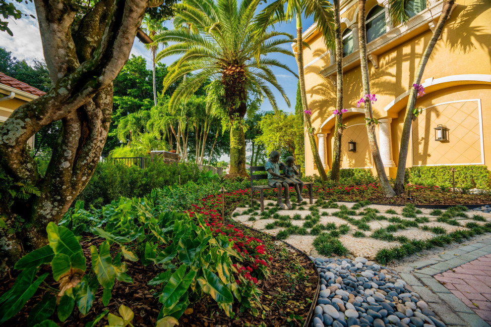 Großer Klassischer Garten im Sommer mit Auffahrt, Steindeko, direkter Sonneneinstrahlung, Flusssteinen und Steinzaun in Miami
