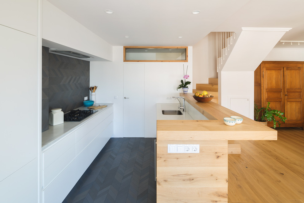 Design ideas for a mid-sized contemporary galley open plan kitchen in Barcelona with an undermount sink, flat-panel cabinets, white cabinets, black splashback, ceramic floors, a peninsula, black floor, panelled appliances and grey benchtop.