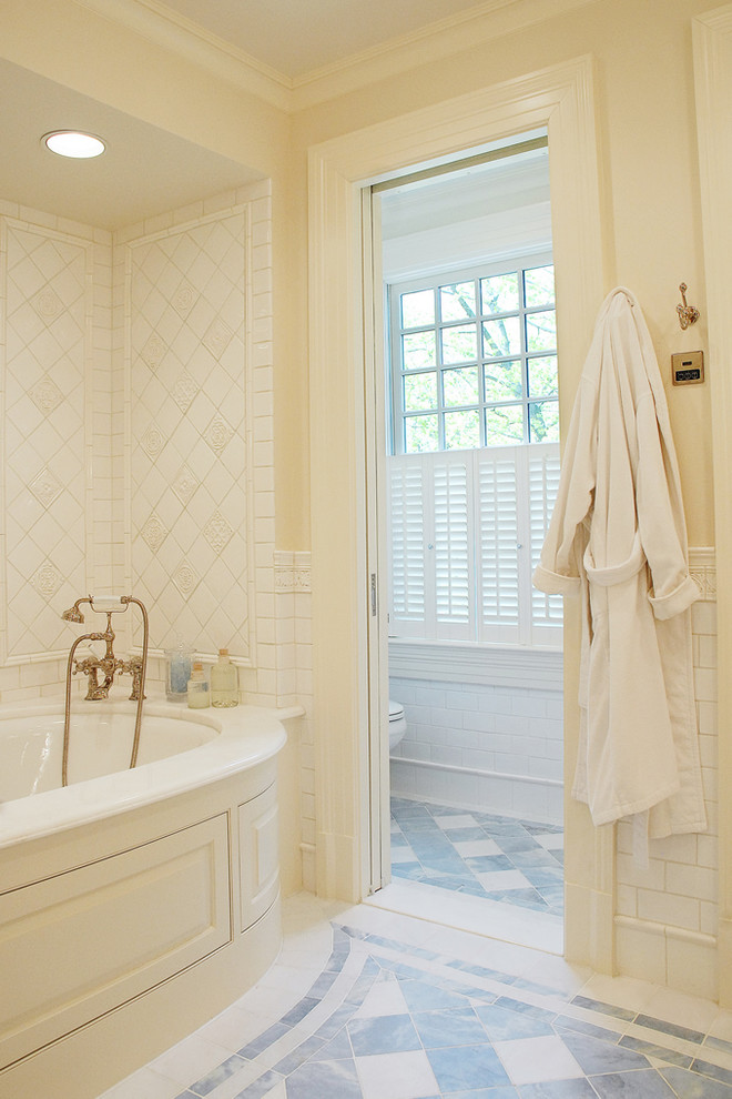 Photo of a large traditional master bathroom in New York with yellow tile, white walls, raised-panel cabinets, beige cabinets, an alcove tub, ceramic tile, ceramic floors, marble benchtops and beige floor.