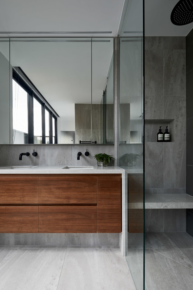 Design ideas for a mid-sized contemporary master bathroom in Melbourne with flat-panel cabinets, medium wood cabinets, gray tile, grey walls, an undermount sink, grey floor, a double shower, a wall-mount toilet, ceramic tile, ceramic floors, engineered quartz benchtops and a sliding shower screen.