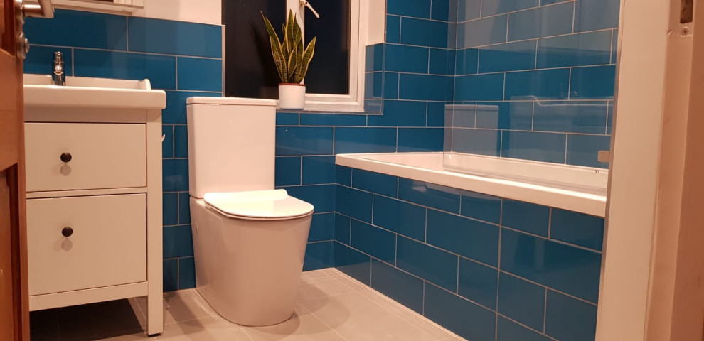 Modern kids bathroom in London with a drop-in tub, a shower/bathtub combo, blue tile, blue walls, ceramic floors and grey floor.