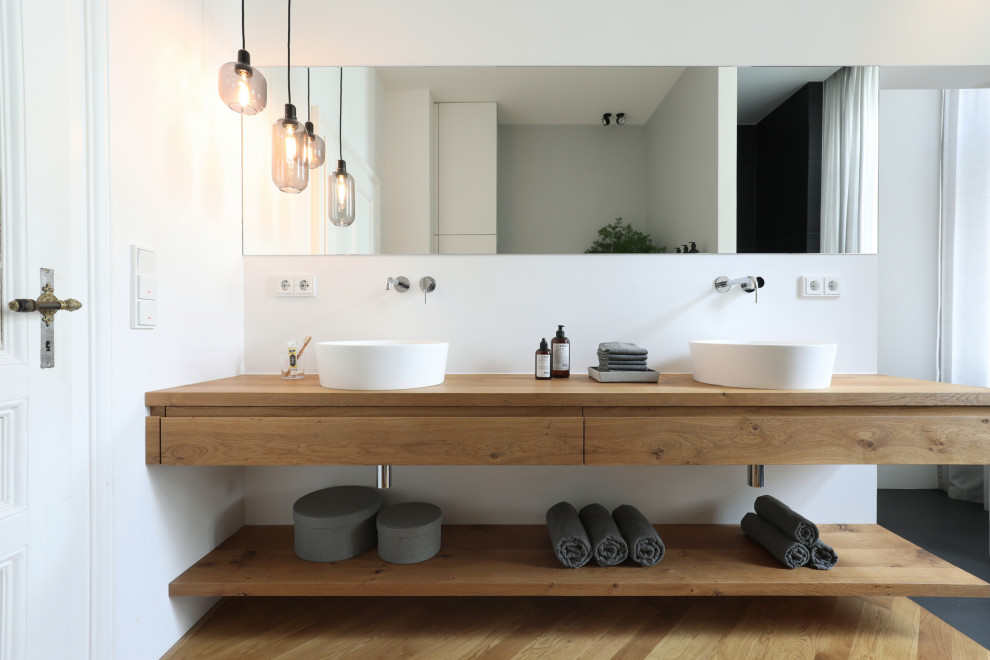 Inspiration for a contemporary bathroom in Frankfurt with flat-panel cabinets, light wood cabinets, a freestanding tub, a curbless shower, a wall-mount toilet, gray tile, light hardwood floors, a vessel sink, solid surface benchtops, grey floor, an open shower, beige benchtops, an enclosed toilet, a double vanity and a floating vanity.