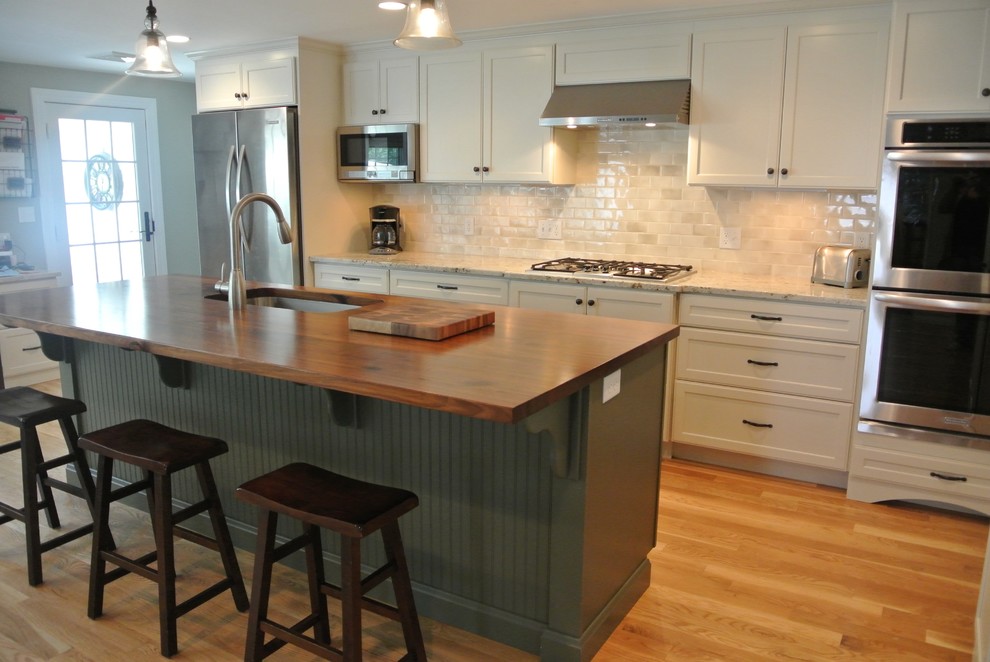 Inspiration for a transitional galley light wood floor eat-in kitchen remodel in Boston with an undermount sink, stainless steel appliances, an island, shaker cabinets, white cabinets, wood countertops, white backsplash, ceramic backsplash and brown countertops