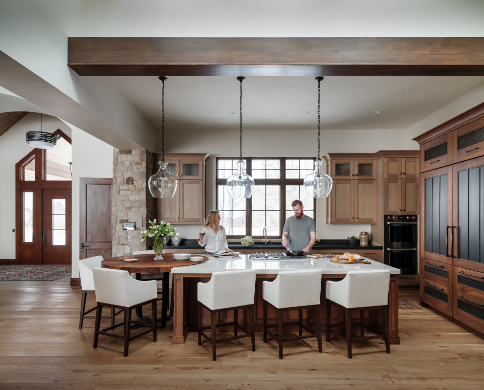 Inspiration for a large country l-shaped eat-in kitchen in Denver with a double-bowl sink, marble benchtops, panelled appliances, light hardwood floors, with island, shaker cabinets, medium wood cabinets, beige floor, black benchtop and exposed beam.