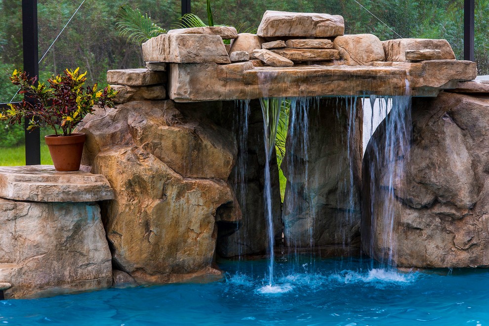 Design ideas for a large tropical backyard custom-shaped natural pool in Tampa with a water feature and natural stone pavers.