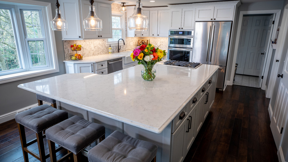 Eat-in kitchen - large transitional u-shaped dark wood floor and brown floor eat-in kitchen idea with a farmhouse sink, recessed-panel cabinets, white cabinets, quartz countertops, white backsplash, marble backsplash, stainless steel appliances, an island and white countertops
