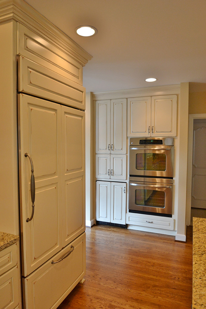 Large transitional l-shaped medium tone wood floor eat-in kitchen photo in Columbus with an undermount sink, raised-panel cabinets, beige cabinets, granite countertops, beige backsplash, paneled appliances and an island
