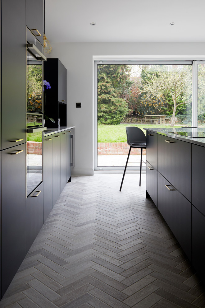 Design ideas for a large contemporary open plan kitchen in Kent with a drop-in sink, flat-panel cabinets, blue cabinets, solid surface benchtops, metallic splashback, glass tile splashback, black appliances, porcelain floors, with island, grey floor and white benchtop.