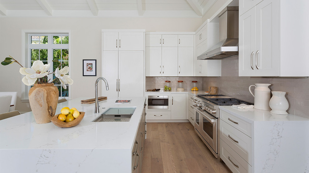 Mid-sized beach style l-shaped open plan kitchen in Miami with a double-bowl sink, brown splashback, subway tile splashback, stainless steel appliances, medium hardwood floors, with island, brown floor, white benchtop, recessed-panel cabinets, white cabinets and marble benchtops.