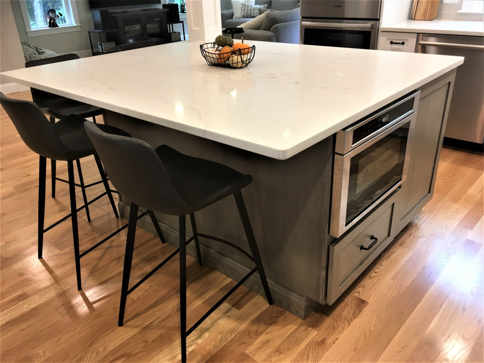 Eat-in kitchen - large transitional u-shaped light wood floor and brown floor eat-in kitchen idea in Boston with a farmhouse sink, shaker cabinets, white cabinets, quartz countertops, beige backsplash, subway tile backsplash, stainless steel appliances, an island and white countertops