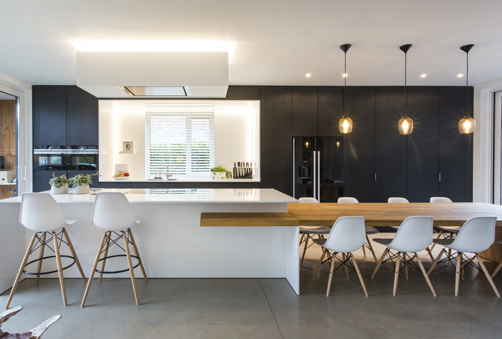 Photo of a midcentury galley kitchen in Other with flat-panel cabinets, black cabinets, black appliances, concrete floors, with island, grey floor and white benchtop.