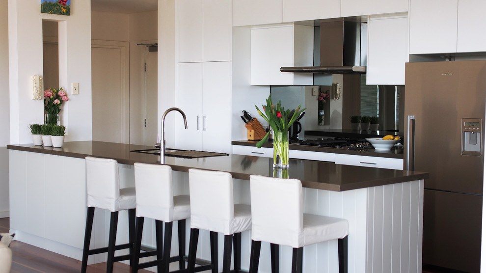 Design ideas for a mid-sized contemporary galley open plan kitchen in Brisbane with an undermount sink, flat-panel cabinets, white cabinets, quartz benchtops, mirror splashback, stainless steel appliances, dark hardwood floors and with island.