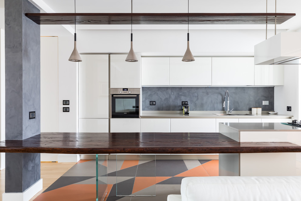 This is an example of a contemporary galley kitchen in Rome with a double-bowl sink, flat-panel cabinets, white cabinets, grey splashback, a peninsula, multi-coloured floor and grey benchtop.