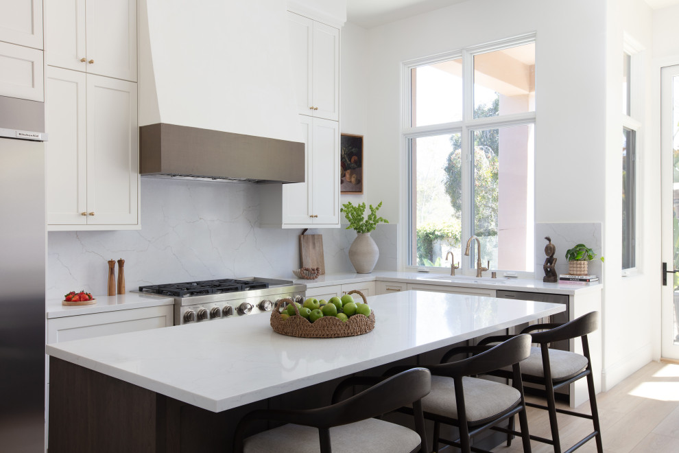 Kitchen - large transitional l-shaped vinyl floor and beige floor kitchen idea in San Diego with an undermount sink, shaker cabinets, quartz countertops, quartz backsplash, stainless steel appliances, an island, white countertops, white cabinets and white backsplash