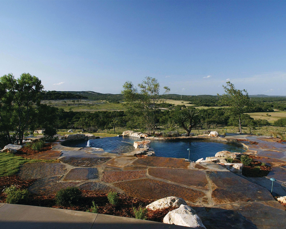 Expansive country backyard custom-shaped natural pool in Austin with a water feature and natural stone pavers.