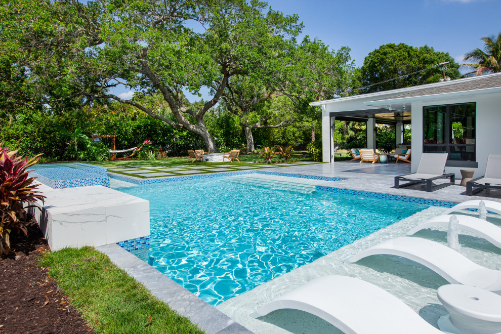 Design ideas for a large midcentury backyard custom-shaped lap pool in Miami with a water feature and natural stone pavers.