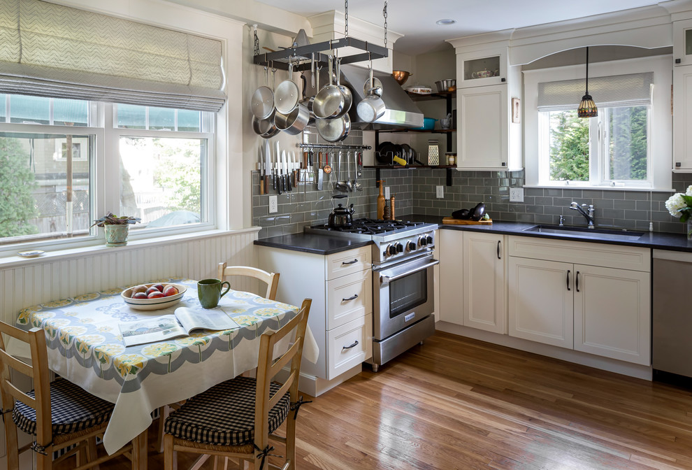 This is an example of a mid-sized traditional l-shaped separate kitchen in Boston with an undermount sink, flat-panel cabinets, white cabinets, quartz benchtops, green splashback, glass tile splashback, stainless steel appliances, medium hardwood floors, no island, brown floor and black benchtop.