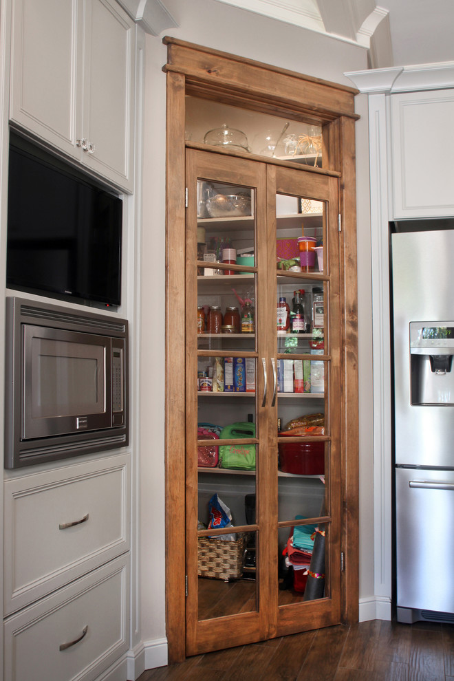 Large transitional l-shaped porcelain tile kitchen pantry photo with a farmhouse sink, recessed-panel cabinets, gray cabinets, granite countertops, white backsplash, glass tile backsplash, stainless steel appliances and an island