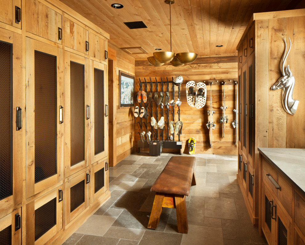 Réalisation d'une grande entrée chalet en bois avec un vestiaire, un sol en ardoise, une porte simple, une porte en bois foncé, un sol gris, un plafond en bois et un mur marron.