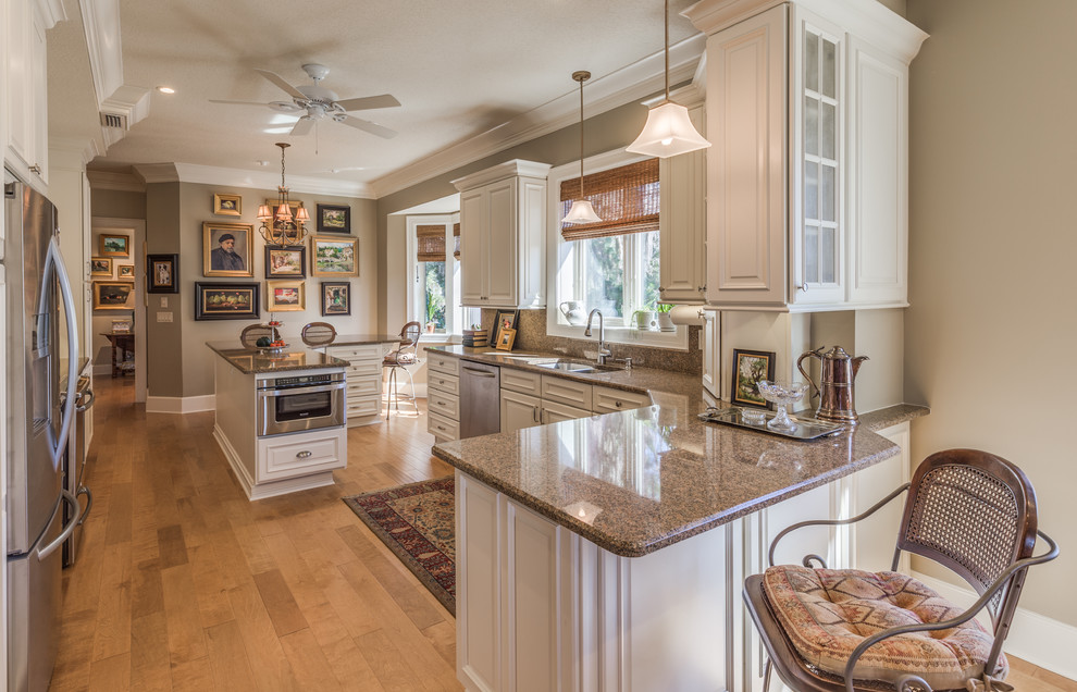 Photo of a traditional u-shaped eat-in kitchen in Jacksonville with an undermount sink, raised-panel cabinets, white cabinets, granite benchtops, beige splashback, stone slab splashback, stainless steel appliances, light hardwood floors and with island.