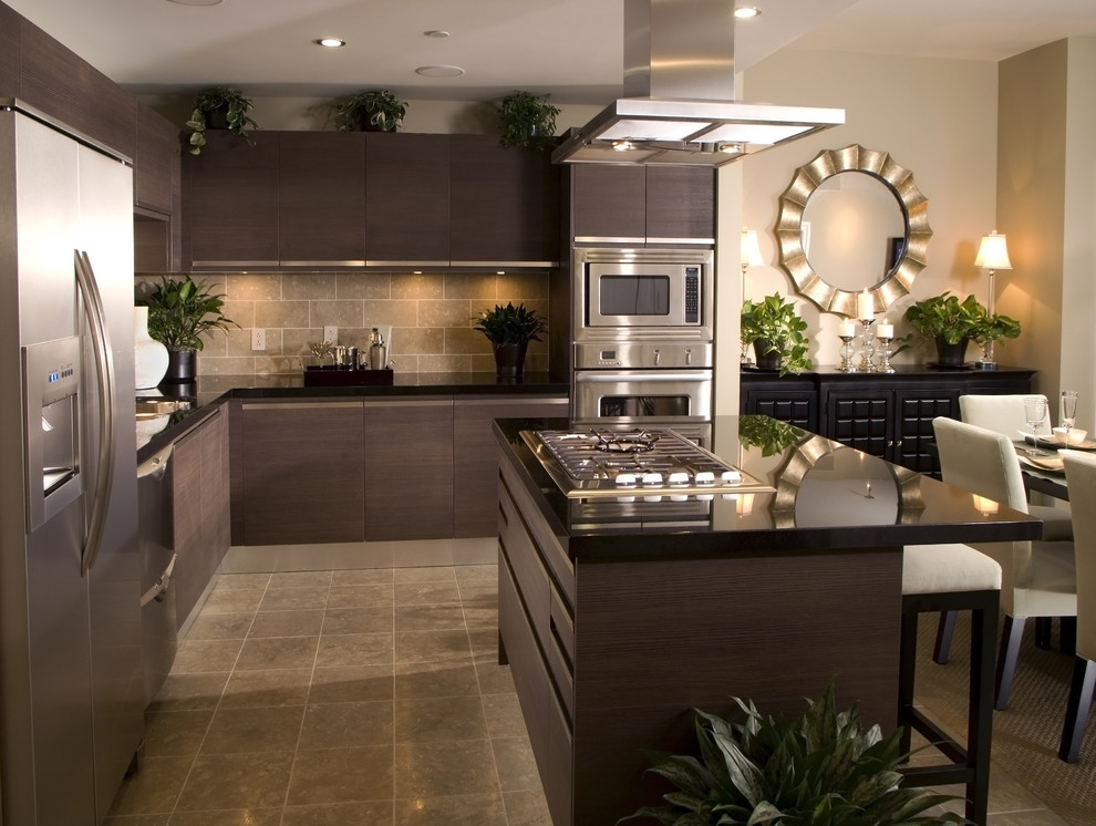 Design ideas for a mid-sized modern l-shaped eat-in kitchen in New York with a double-bowl sink, flat-panel cabinets, dark wood cabinets, granite benchtops, beige splashback, travertine splashback, stainless steel appliances, travertine floors, with island, beige floor and black benchtop.
