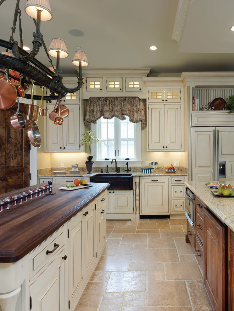This is an example of a large country single-wall separate kitchen in DC Metro with a farmhouse sink, raised-panel cabinets, white cabinets, granite benchtops, beige splashback, stone tile splashback, panelled appliances, travertine floors, multiple islands and beige floor.