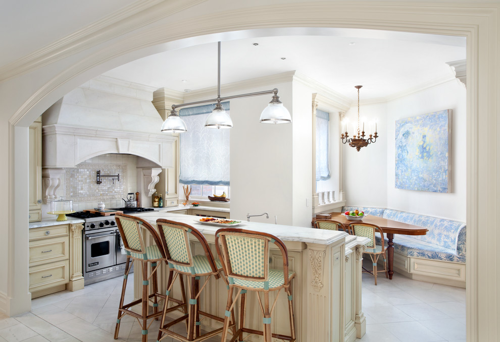 This is an example of a mid-sized traditional u-shaped eat-in kitchen in New York with an undermount sink, recessed-panel cabinets, beige cabinets, marble benchtops, white splashback, mosaic tile splashback, stainless steel appliances, limestone floors and with island.